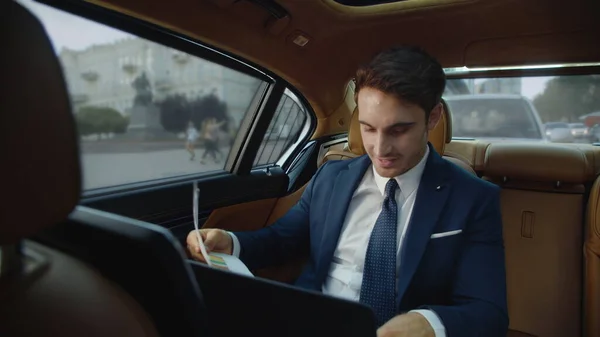 Young male professional looking at data documents in business car. Man in car
