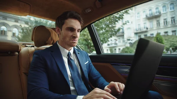 Kızgın erkek CEO, lüks bir arabada dizüstü bilgisayar kullanıyor. İş adamı kızgın hissediyor