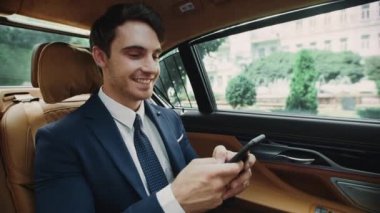 İş arabasında akıllı telefondan mesaj yazan gülümseyen iş adamının portresi.