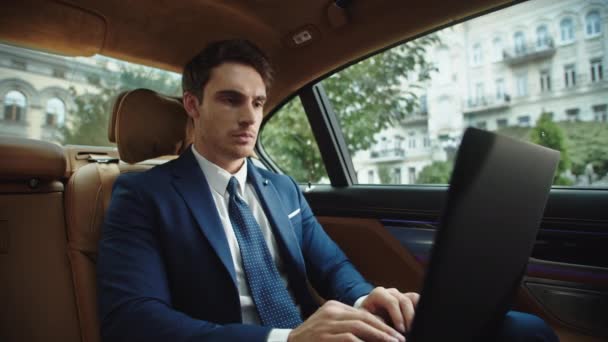 Portret skupionego biznesmena piszącego na laptopie w nowoczesnym samochodzie. — Wideo stockowe