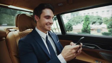 Neşeli iş adamı lüks arabasıyla akıllı telefondan mesaj yazıyor..