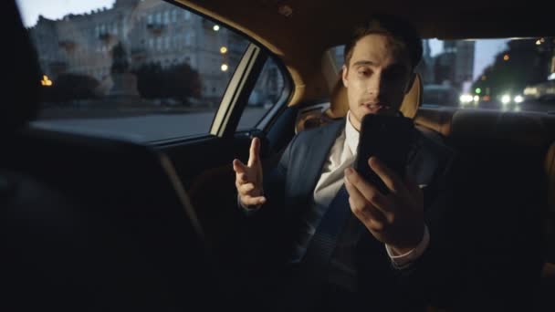 Amistoso hombre de negocios hablando en videollamada en el teléfono en el coche oscuro de negocios. — Vídeos de Stock