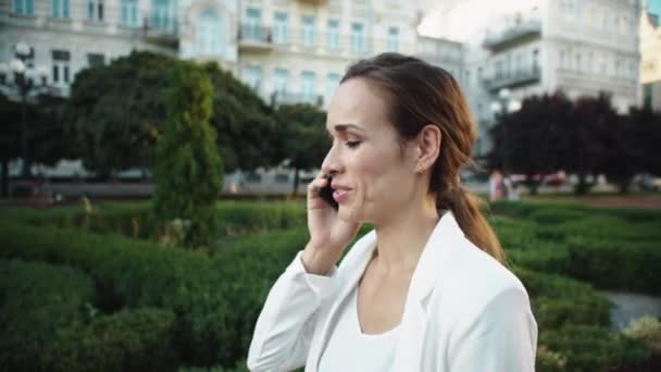 Porträt einer lächelnden Frau, die beim Stadtspaziergang mit dem Smartphone spricht. — Stockvideo
