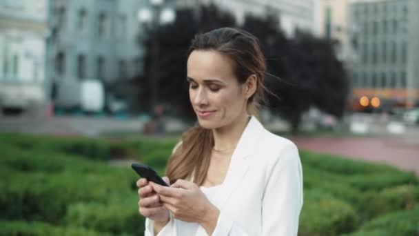 도시 산책을 하면서 전문적 인 여성들이 전화로 글을 쓰며 웃는 모습. — 비디오