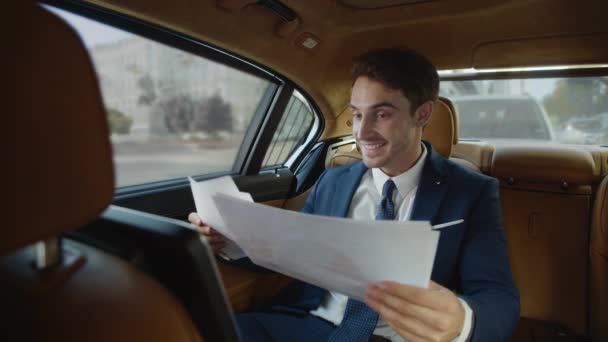 Uśmiechnięty mężczyzna profesjonalny radujący się z dobrych wyników w papierkowej robocie w samochodzie służbowym. — Wideo stockowe