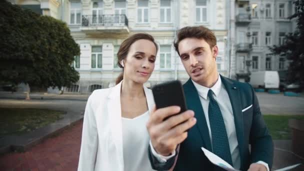 Friendly business man showing smiling woman information on phone on city walk. — Stock video