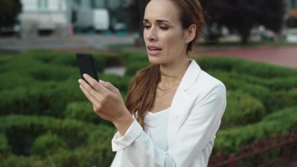 Amistosa mujer de negocios hablando en videollamada en smartphone en la ciudad a pie. — Vídeo de stock