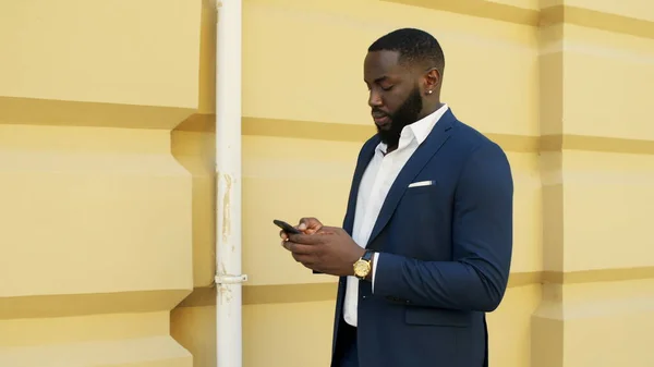Serious african businessman texting outdoors. Businessman writing message