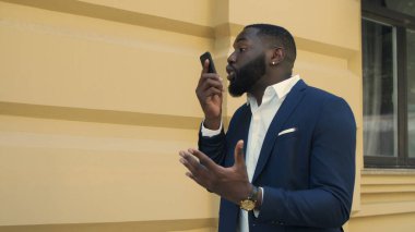 İş adamı akıllı telefonuyla dışarı çıkıyor. Telefonda konuşan afro adam..