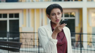 Odaklanmış melez kadın dışarıda telefon görüşmesi yapıyor. Hoparlörden konuşan bayan.