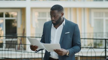 Afro işadamı dışarıda belgeleri inceliyor. Odaklanmış Afrikalı adam kağıtlara bakıyor.