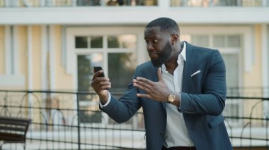 Sinirli iş adamı şehir sokağında görüntülü konuşma yapıyor. Dışarıda dikilen adam