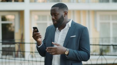 Kendine güvenen erkek profesyonel dışarıda görüntülü konuşma yapıyor. Dışarıda dikilen adam