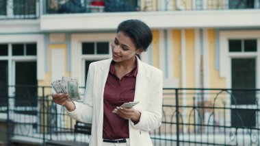 Dışarıda dolarlar sayan zengin melez kadın. İş kadını para yığını tutuyor