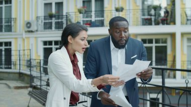 Dışarıda verileri inceleyen sinirli yöneticiler. Karışık ırk çiftleri projeyi tartışıyor