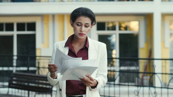 Businesswoman reading documents at urban street. Woman looking project papers