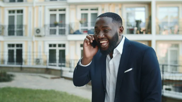 Emotional african businessman calling smartphone outdoors. Man talking phone