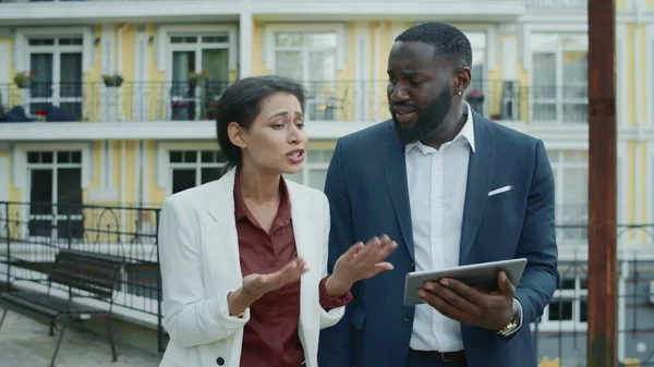 Sad mixed race partners talking at street. Upset businesswoman sharing news