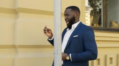 Gülümseyen iş adamı şehir sokaklarında nakit parayla oynuyor. Afro adam dışarıda yürüyor.