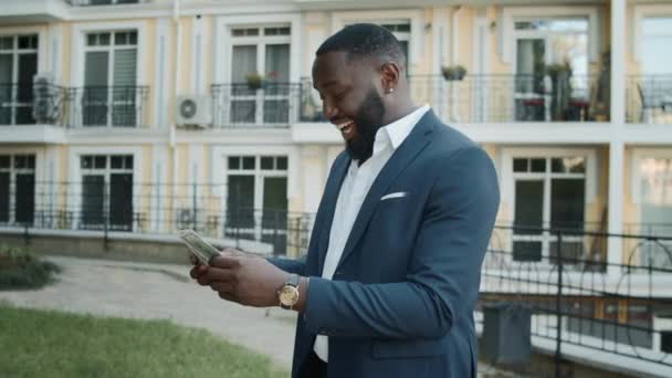 Un hombre de negocios africano reteniendo dinero afuera. Hombre alegre contando dinero al aire libre — Vídeos de Stock