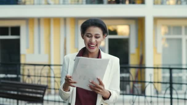 Fröhliche Geschäftsfrau mit gemischtem Rasse, die in der städtischen Straße Dokumente liest. Dame im Freien — Stockvideo