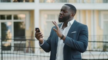 Afro iş adamı dışarıda görüntülü konuşma yapıyor. Afrikalı adam dışarıda telefonla konuşuyor.