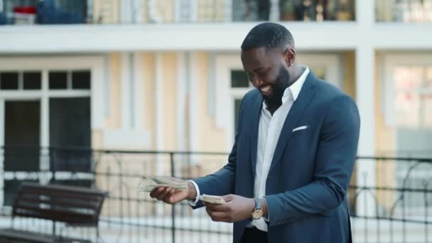 Cheerful businessman smelling dollars at urban street. Afro guy holding cash — Stock Video