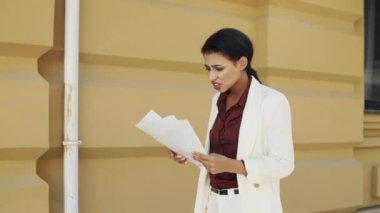 Kafası karışmış bir iş kadını dışarıda doktor okuyor. Genç bir kadın dışarıda yürüyor.