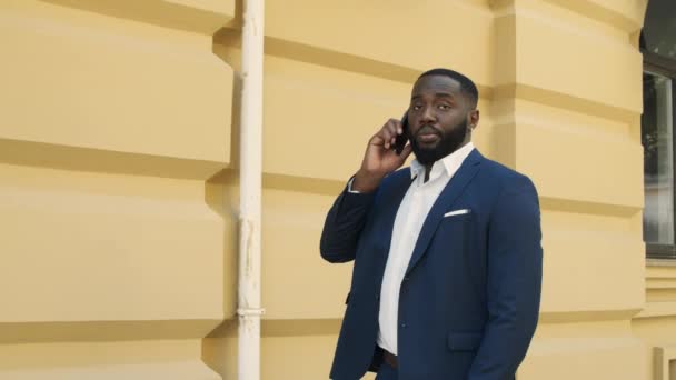 Empresario africano caminando por la calle. Joven hombre de negocios afro hablando en el móvil — Vídeos de Stock