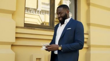 Gülümseyen afro adam dışarıda para sayıyor. İş adamı dışarıda parayla yürüyor.