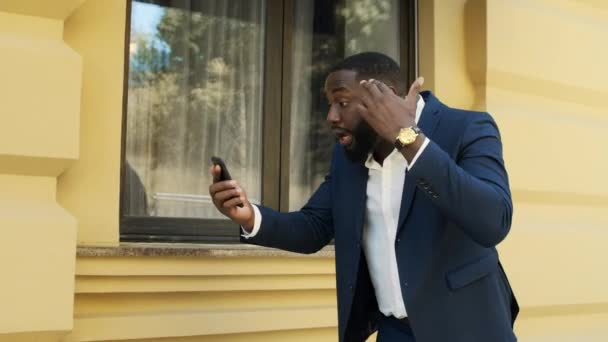 Réfléchi afro gars parlant au téléphone. Homme d'affaires faisant des gestes à l'extérieur — Video
