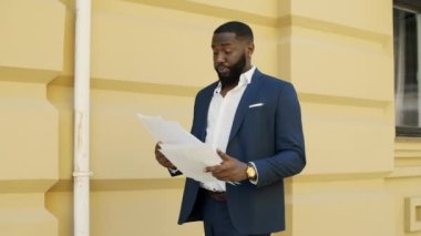 Afrikalı işadamı şehir sokaklarındaki belgeleri kontrol ediyor. Afro adam dışarıda yürüyor..