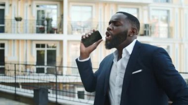 Mutlu Afrikalı işadamı dışarıda telefonla dans ediyor. Kazanan afro adam dans ediyor.