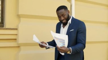 Afrikalı işadamı dışarıda gazete okuyor. Afro adam dışarıda belgeleri kontrol ediyor.