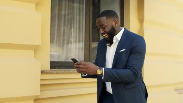 Mosolygó afro üzletember sms-ezik a szabadban. Afro man üzeneteket olvas — Stock videók