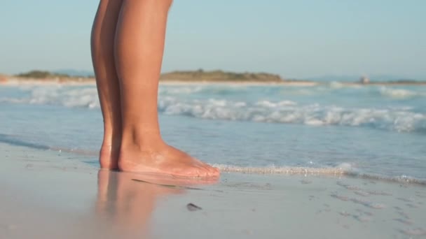 Fale morskie pędzące do kobiecych nóg na plaży. Nieznana dziewczyna stojąca nad brzegiem morza. — Wideo stockowe