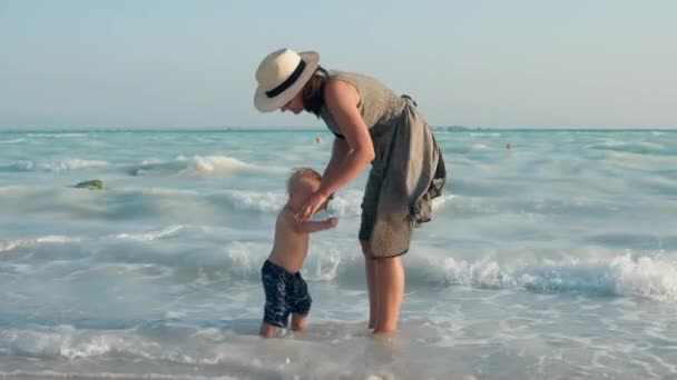 Szczęśliwa matka i dziecko wychodzą z wody na wybrzeżu. słodkie dziecko siedzi w wodzie. — Wideo stockowe