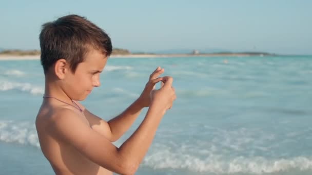 Chłopak robi zdjęcia na komórce nad morzem. Facet filmujący na smartfonie na plaży. — Wideo stockowe