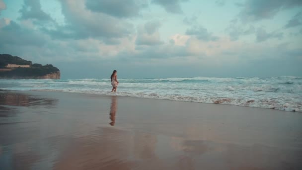 Ευτυχισμένο κορίτσι που απολαμβάνει το πρωινό στην παραλία. Νεαρή γυναίκα που κοιτάζει τα κύματα στο θαλάσσιο σερφ — Αρχείο Βίντεο