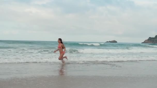 Młoda kobieta spędzająca lato nad morzem. Wesoła dziewczyna biegnie wzdłuż plaży. — Wideo stockowe