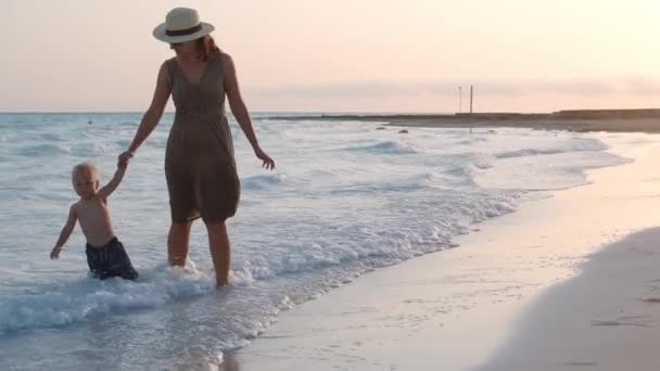 妈妈在海滩上牵着小手.妈妈和儿子在海岸线享受日落. — 图库视频影像