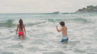 Deniz kenarında yüzen gülümseyen gençler. Dalgalar halinde oynayan mutlu çocuklar.