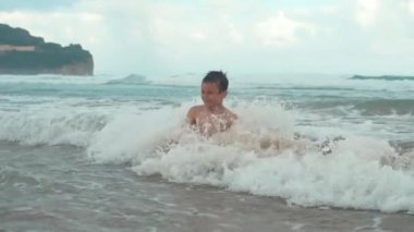 Neşeli çocuk deniz kıyısında vakit geçiriyor. Neşeli genç su sıçratıyor..