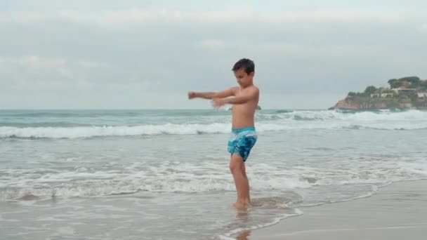 Щасливий хлопчик проводить літні канікули на морі. Хлопець робить вправи на узбережжі . — стокове відео