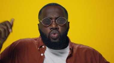 Sarı arka planda dans eden Afro-Amerikan bir adamın portresi. Adam eğleniyor.