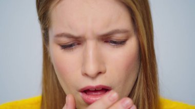 Gri arka planda kameraya öksüren hasta bir genç kadın. Bayan kendini kötü hissediyor