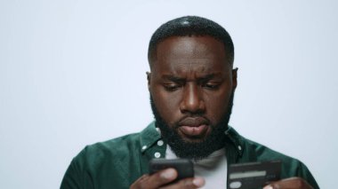 Odaklanmış Afrikalı adam stüdyoda akıllı telefondan başarılı bir şekilde alışveriş yapıyor..