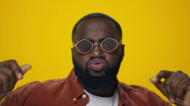 Güneş gözlüklü neşeli Afrikalı Amerikalı adam sarı arka planda dans ediyor..