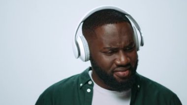 Yakından gülümseyen Afrikalı adam gri arka planda kulaklıkla müzik dinliyor..