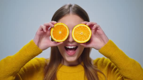 Retrato de mulher alegre se divertindo com duas fatias de laranja no estúdio. — Vídeo de Stock